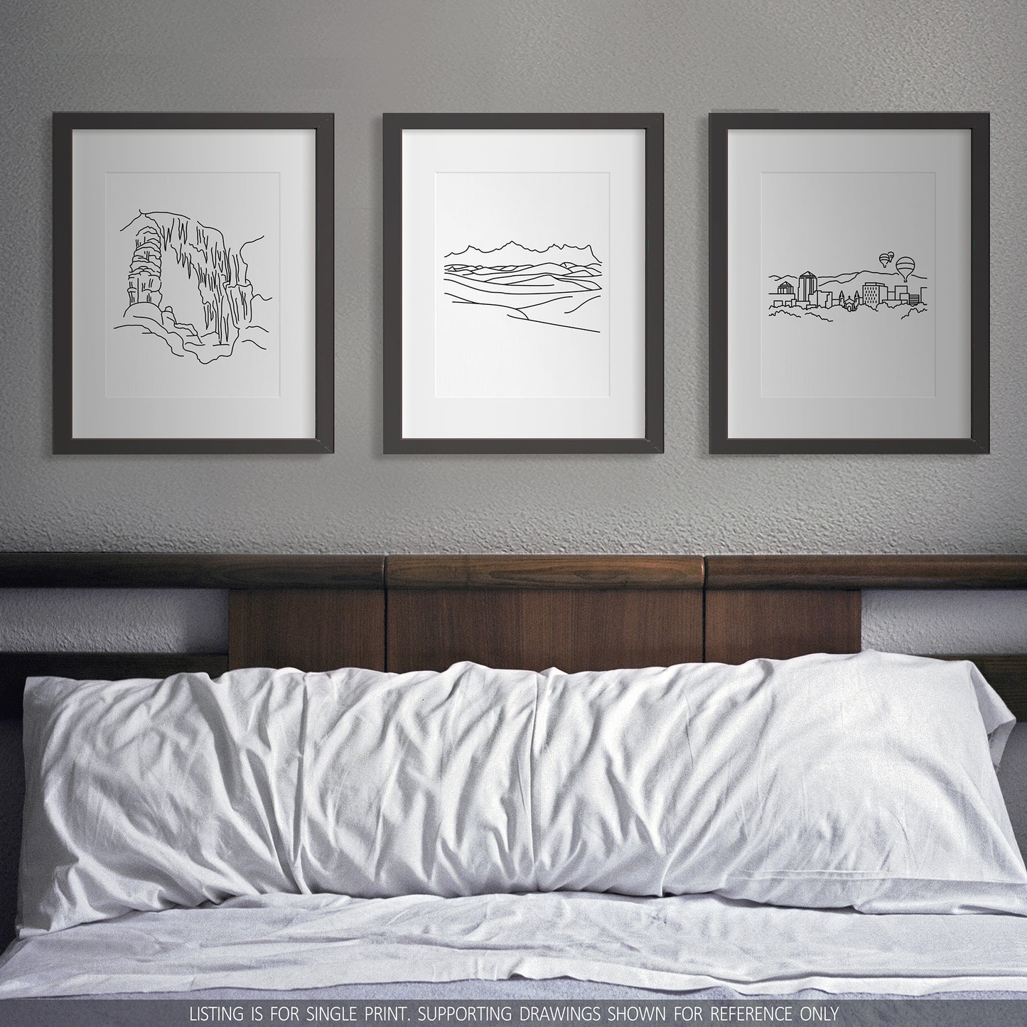 A group of three framed drawings on a wall above a bed. The line art drawings include Carlsbad Caverns National Park, White Sands National Park, and the Albuquerque Skyline