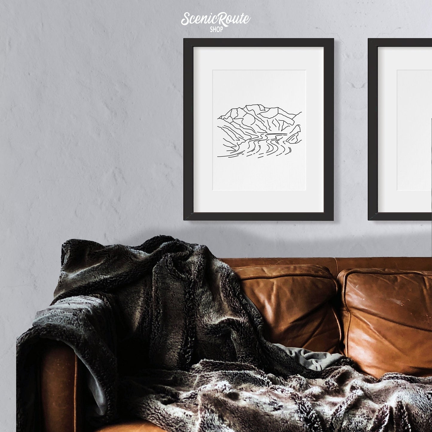 A framed line art drawing of Wrangell Saint Elias National Park above a couch with a blanket