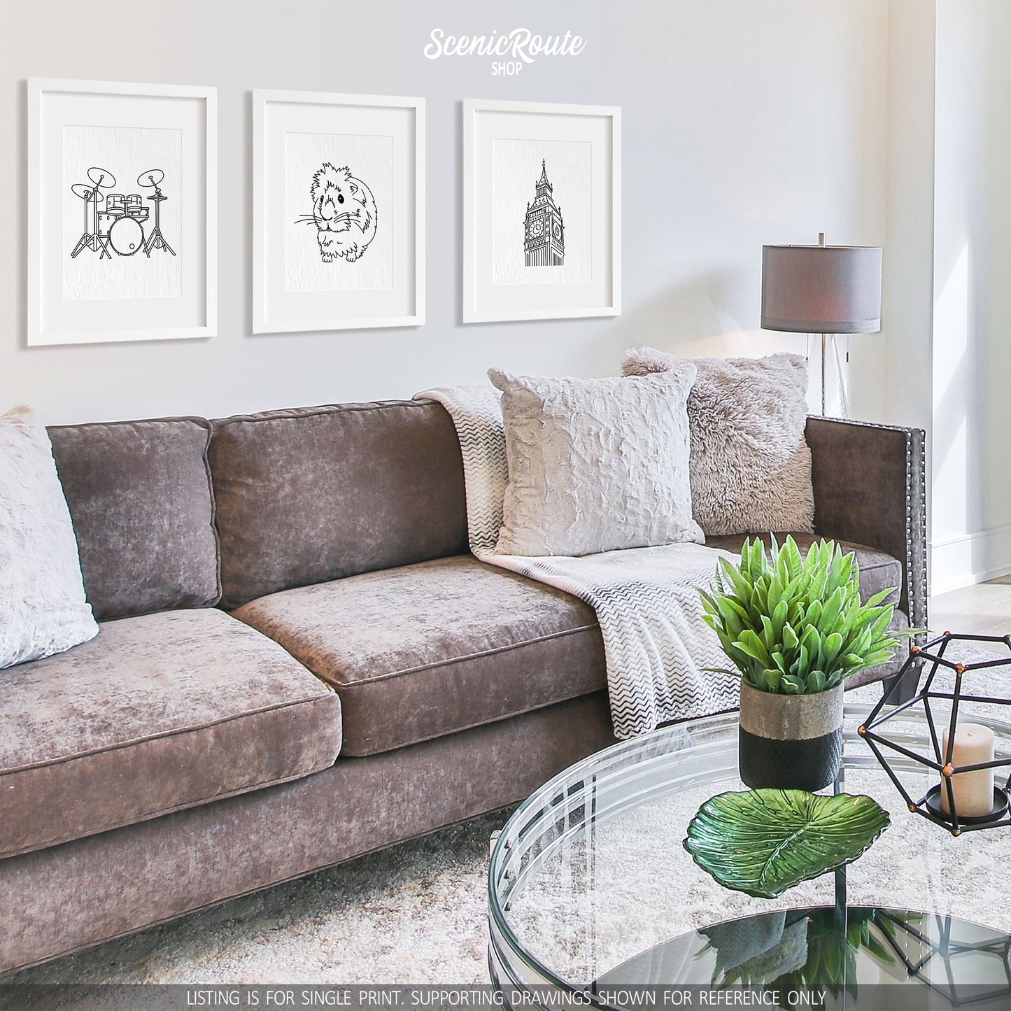A group of three framed drawings on a white wall hanging above a couch with pillows and a blanket. The line art drawings include Drums, Guinea Pig, and Big Ben