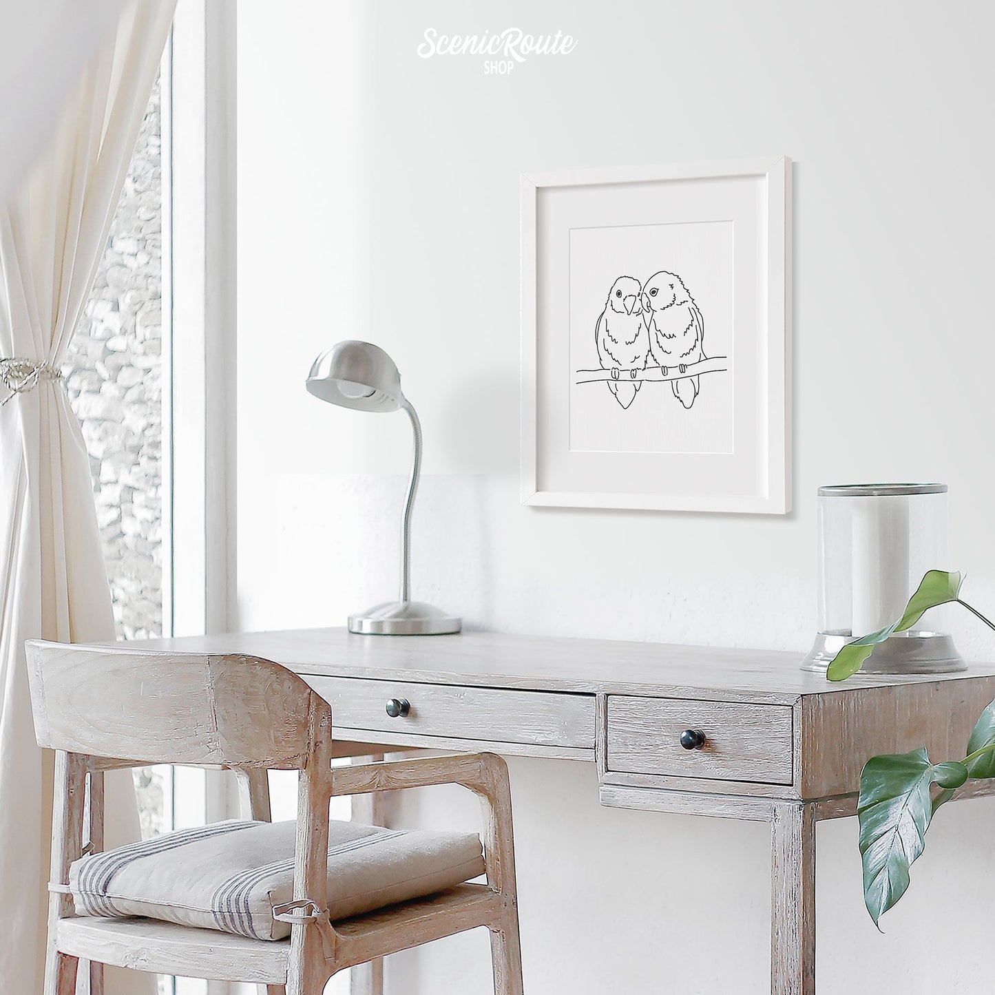 A framed line art drawing of a Love Birds on a white wall above a desk.
