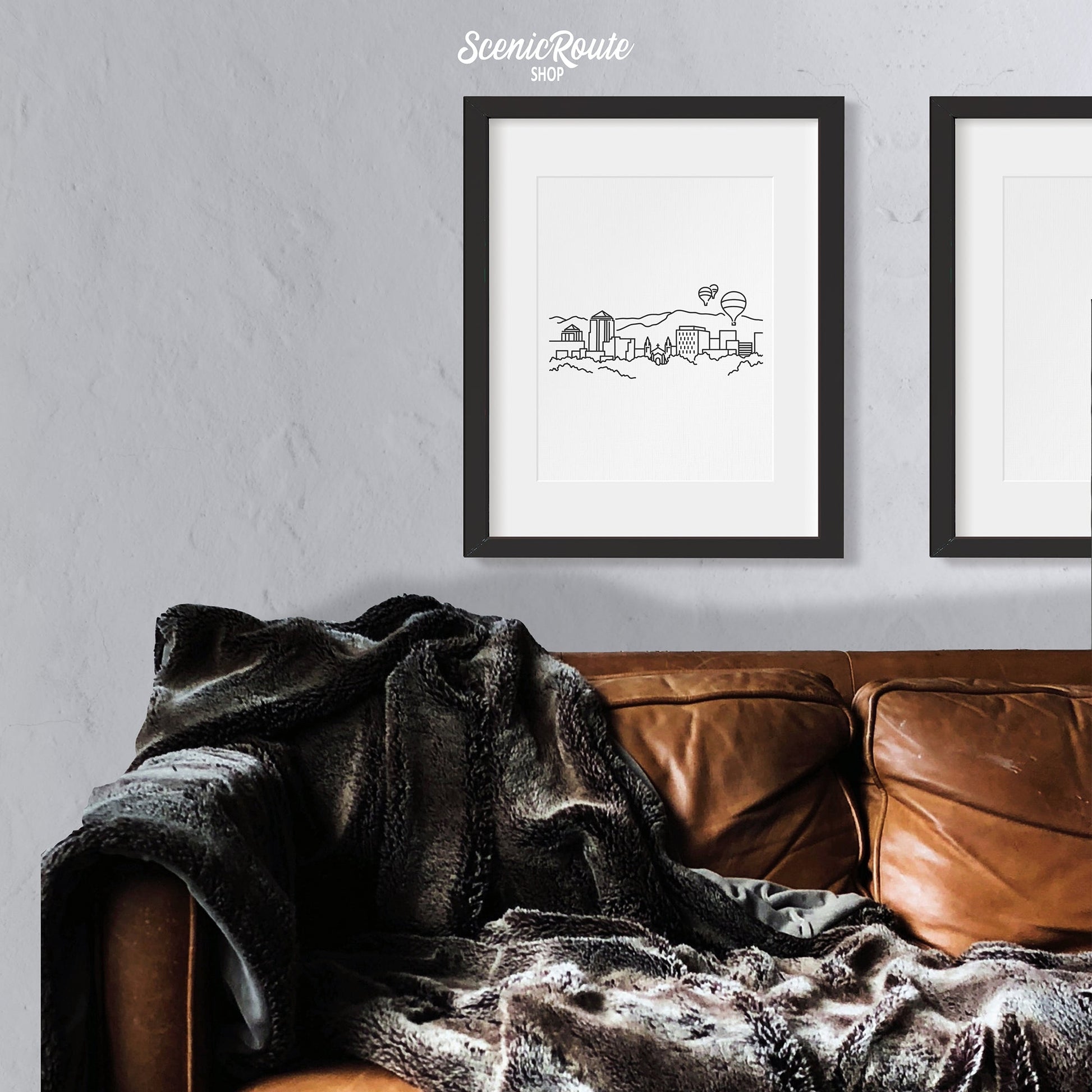 A framed line art drawing of the Albuquerque Skyline hung above a couch with a blanket