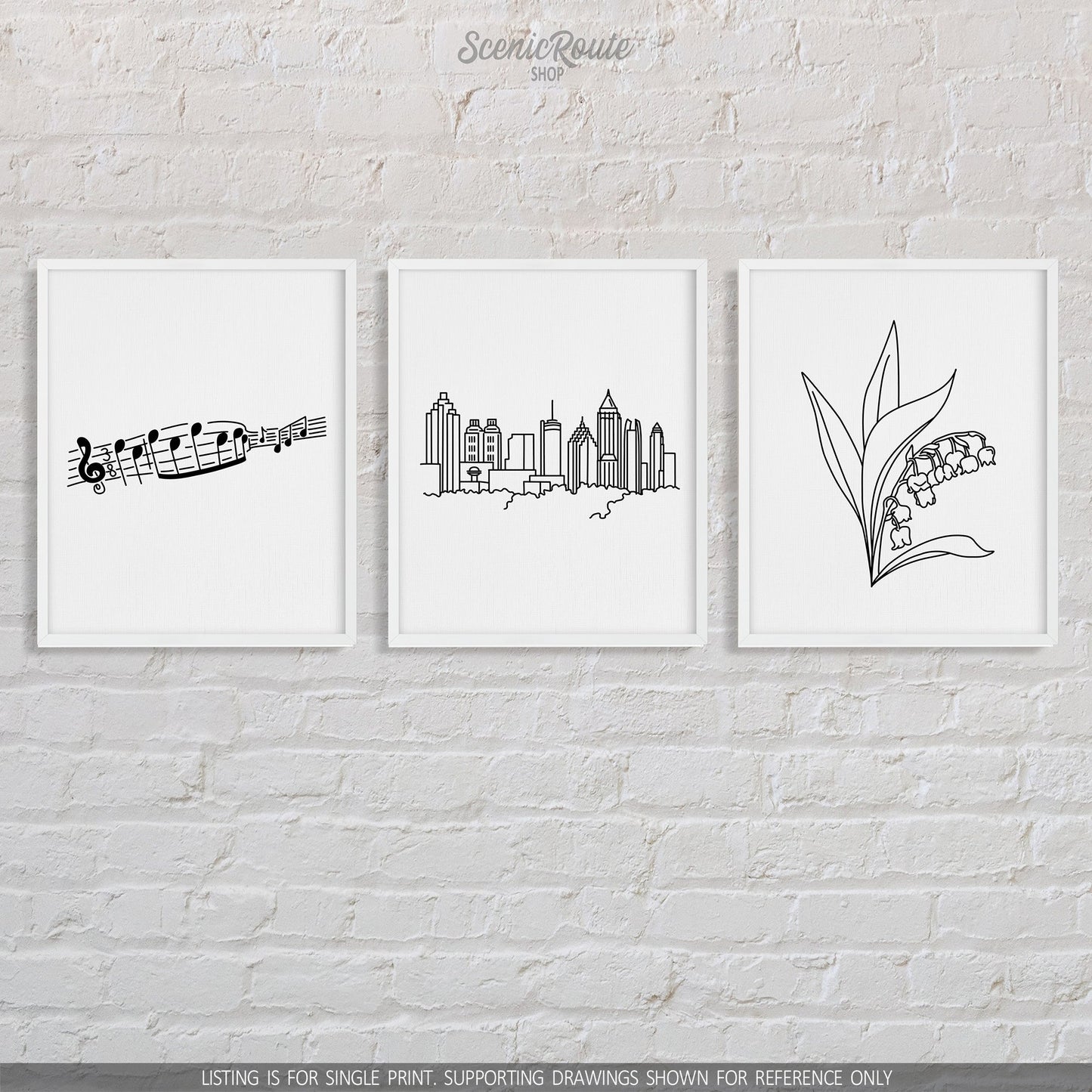 A group of three framed drawings on a brick wall. The line art drawings include Music Notes, the Atlanta Skyline, and a Lily of the Valley Flower