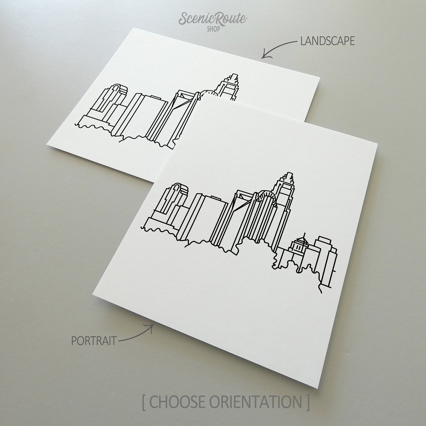 Two line art drawings of the Charlotte Skyline on white linen paper with a gray background.  The pieces are shown in portrait and landscape orientation for the available art print options.