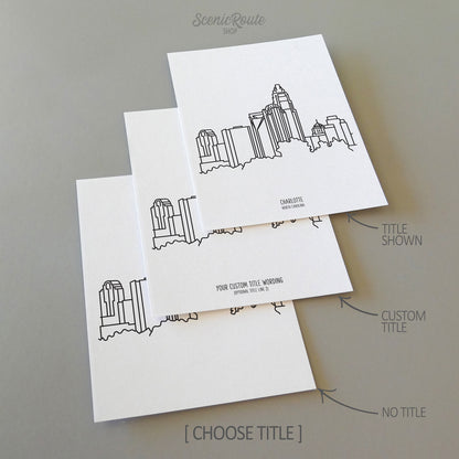 Three line art drawings of the Charlotte North Carolina Skyline on white linen paper with a gray background. The pieces are shown with title options that can be chosen and personalized.