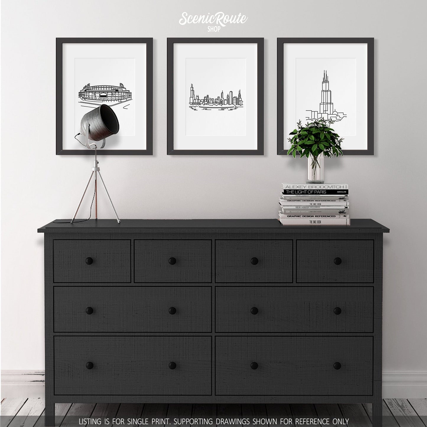 A group of three framed drawings on a wall above a dresser with books and a plant. The line art drawings include Wrigley Field, the Chicago Skyline, and the Willis Tower