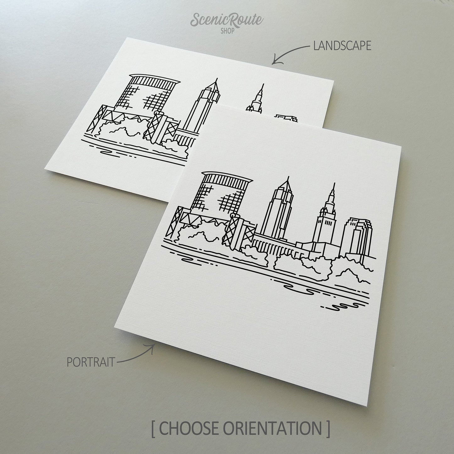 Two line art drawings of the Cleveland Skyline on white linen paper with a gray background. The pieces are shown in portrait and landscape orientation for the available art print options.