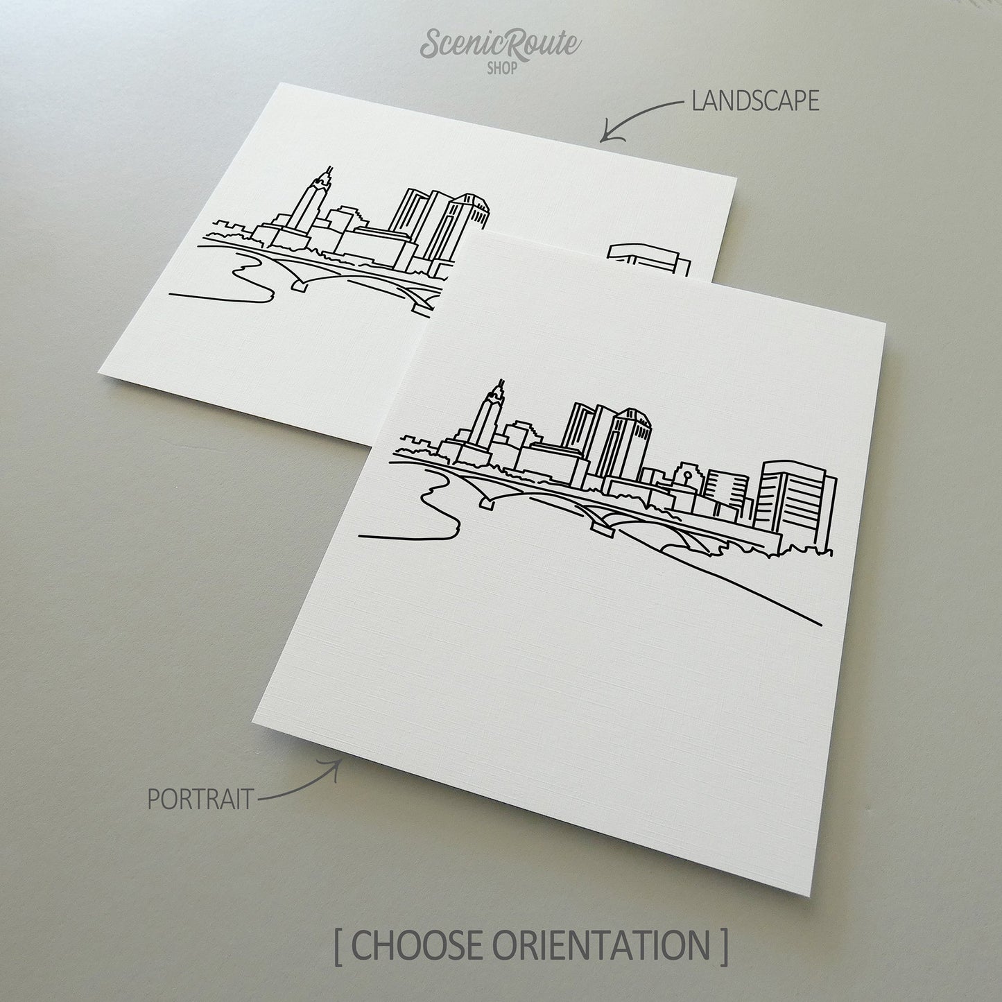 Two line art drawings of the Columbus Skyline on white linen paper with a gray background.  The pieces are shown in portrait and landscape orientation for the available art print options.