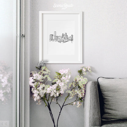 A framed line art drawing of the Houston Skyline hanging above a flowering plant