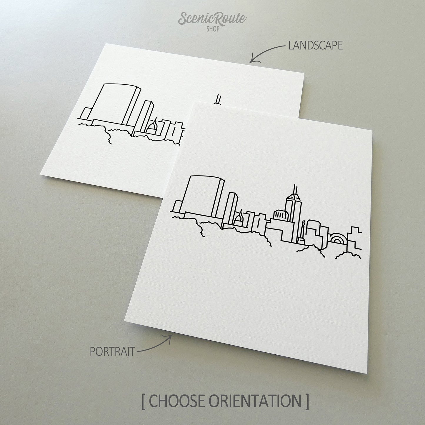 Two line art drawings of the Indianapolis Skyline on white linen paper with a gray background.  The pieces are shown in portrait and landscape orientation for the available art print options.