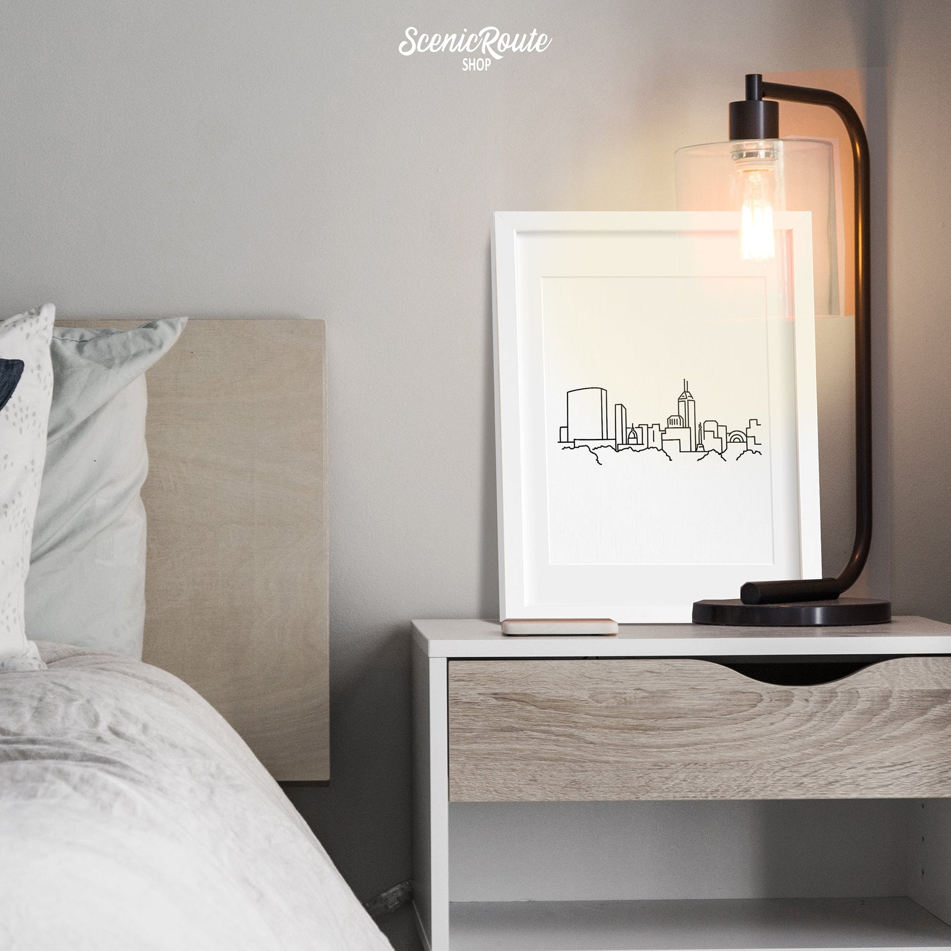 A framed line art drawing of the Indianapolis Skyline above a nightstand next to a bed