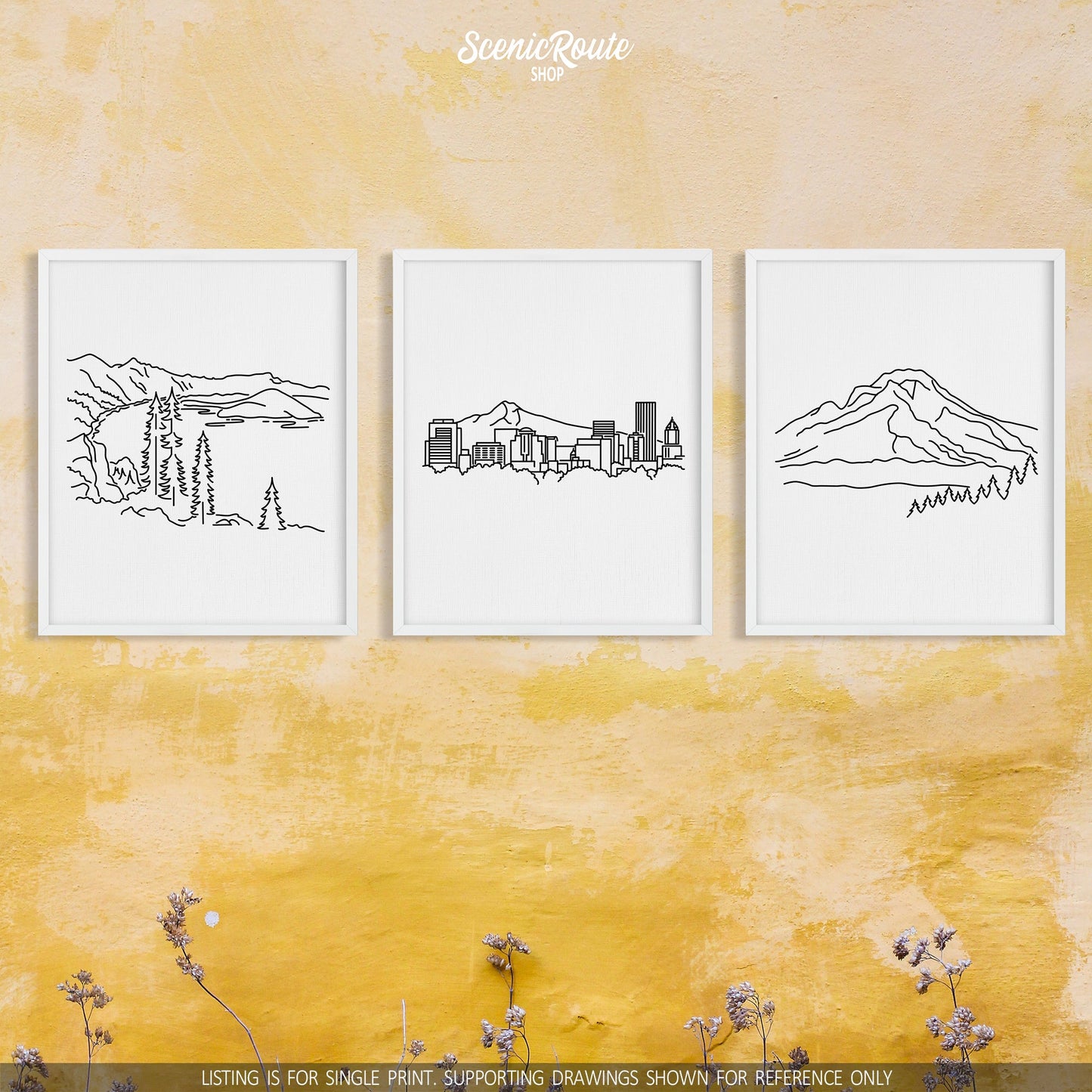 A group of three framed drawings on a yellow wall. The line art drawings include Crater Lake National Park, the Portland Skyline, and Mount Hood