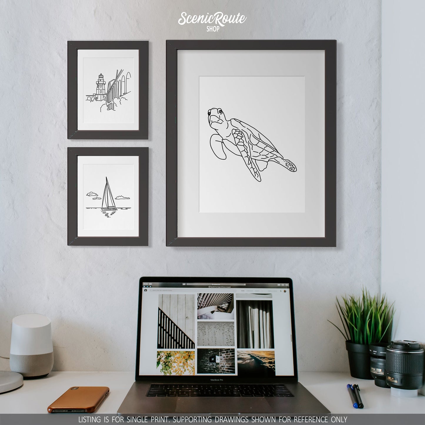 A group of three framed drawings on a white wall above a desk and laptop. The line art drawings include Dry Tortugas National Park, Sailing, and a Sea Turtle
