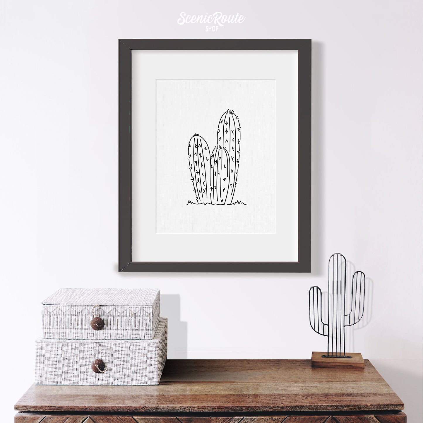 A framed line art drawing of a Torch Cactus hanging above a table with cactus figurine
