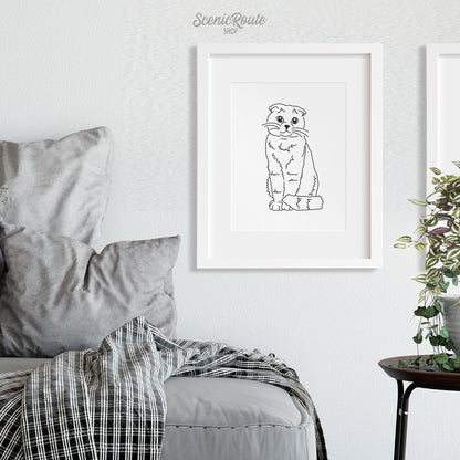 A framed line art drawing of a Scottish Fold cat on a white wall above a couch.