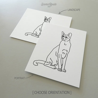 Two line art drawings of a Siamese cat on white linen paper with a gray background.  The pieces are shown in portrait and landscape orientation for the available art print options.