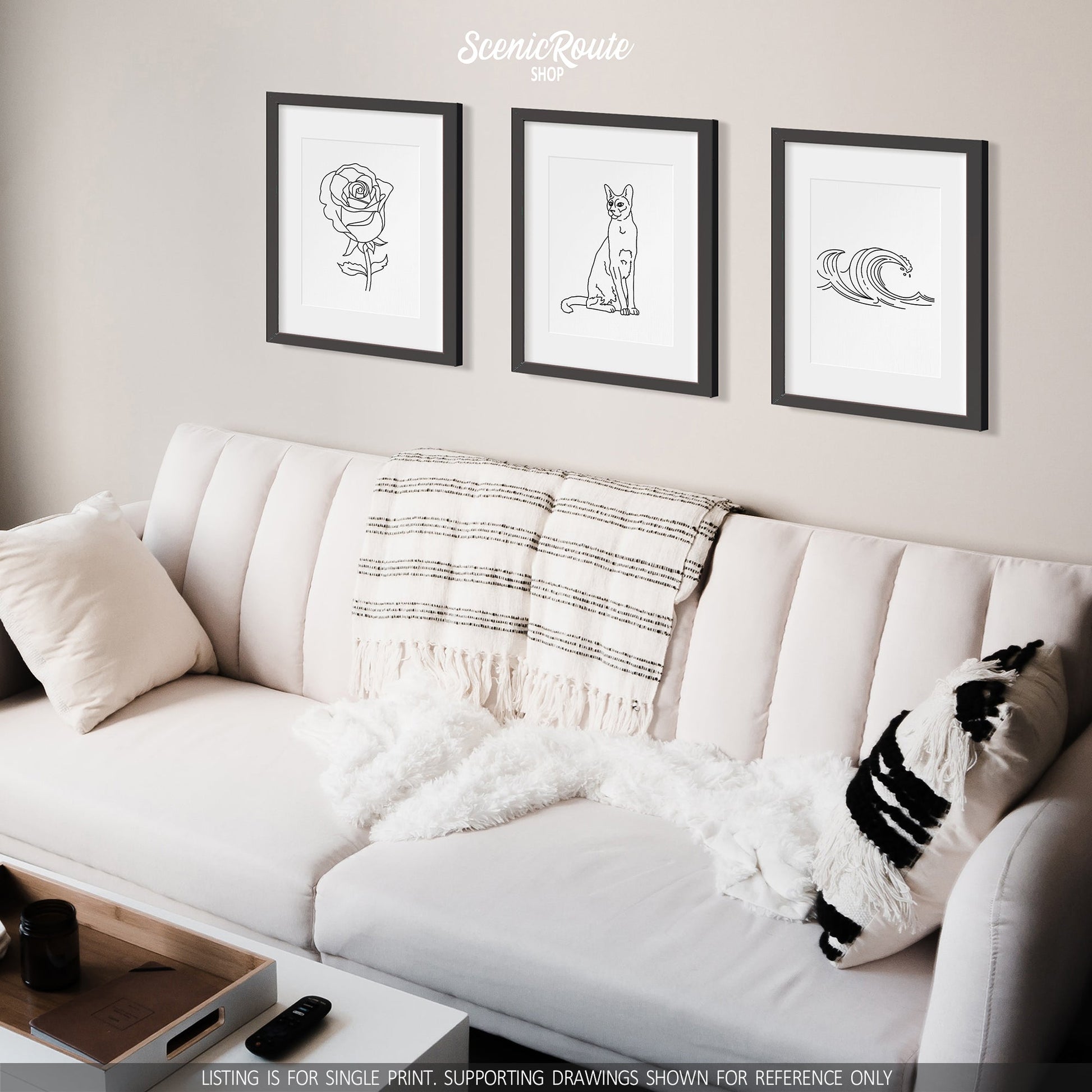 A group of three framed drawings on a wall above a couch. The line art drawings include a Rose Flower, Siamese cat, and Waves
