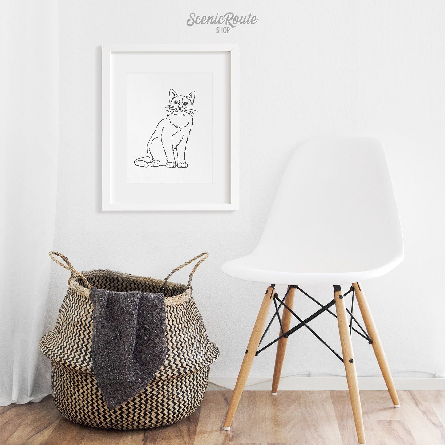 A framed line art drawing of a Snowshoe cat above a basket and chair
