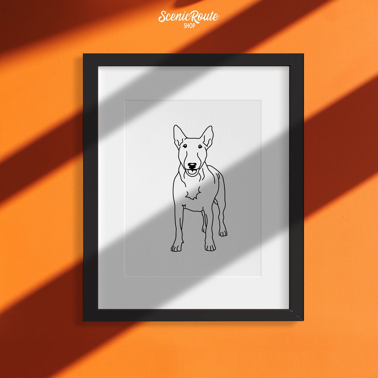 A framed line art drawing of a Bull Terrier on an orange wall with sun shadows
