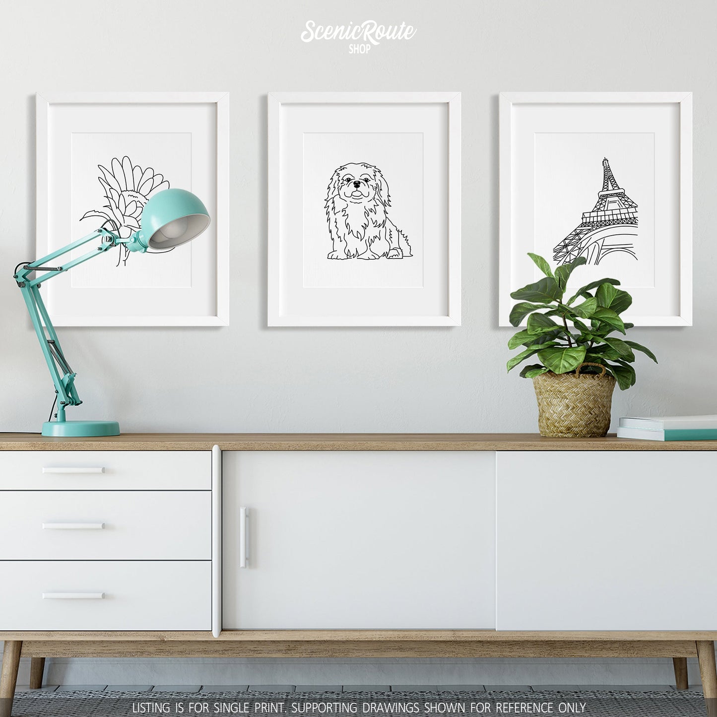 A group of three framed drawings on a white wall above a credenza with a lamp and plant. The line art drawings include a Sunflower, a Pekingese dog, and the Eiffel Tower