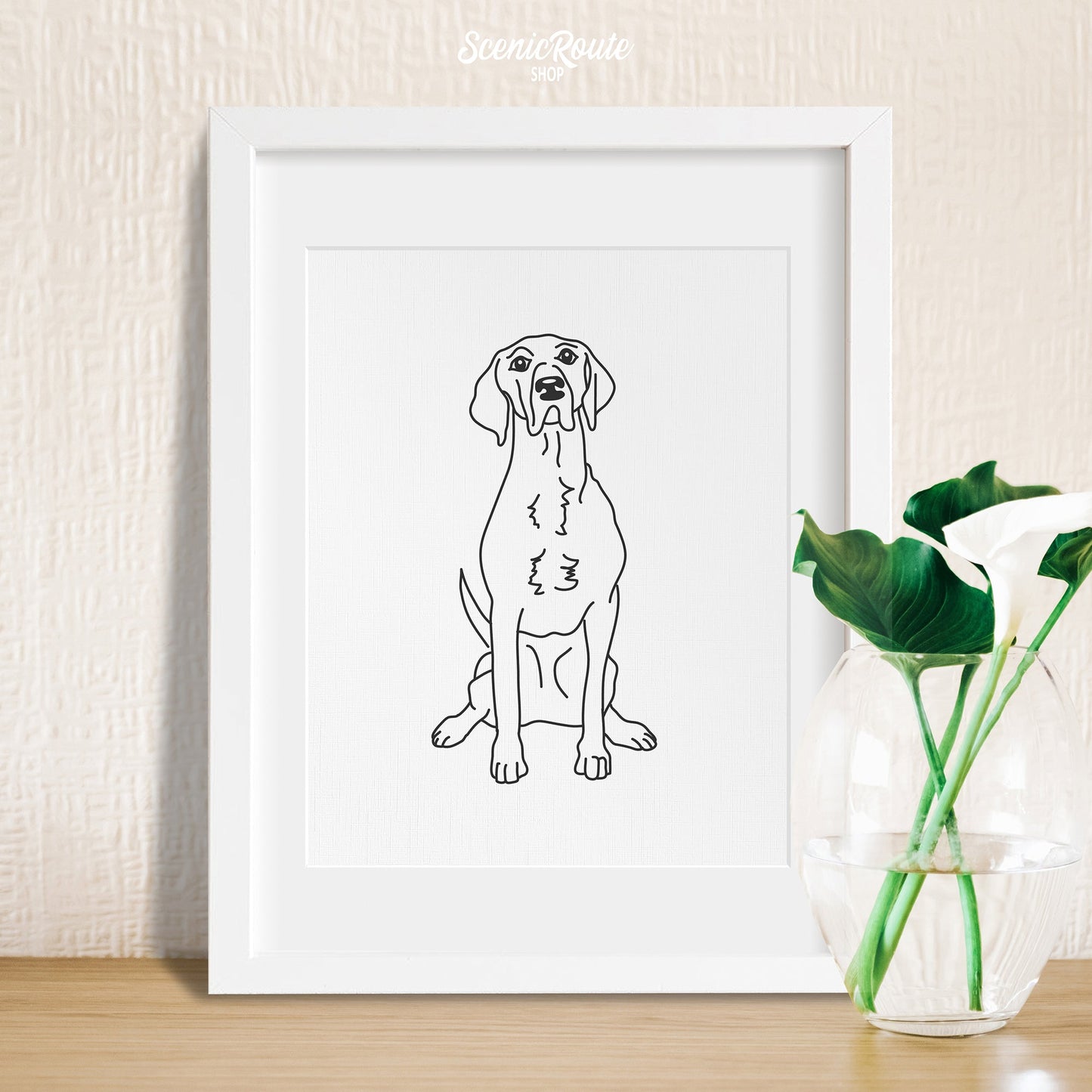 A framed line art drawing of a Pointer dog on a table with a plant