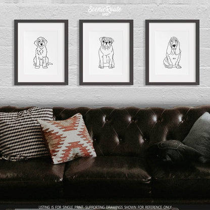 A group of three framed drawings on a white wall above a dark leather couch with pillows. The line art drawings include a Goldendoodle dog, a Pug dog, and a Basset Hound dog