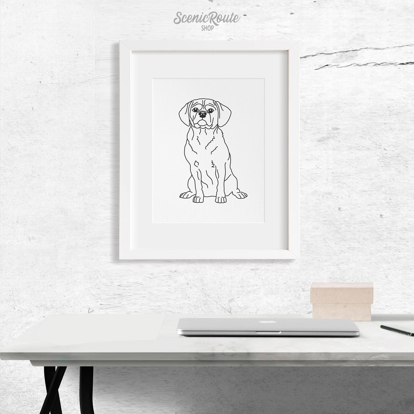 A framed line art drawing of a Puggle dog above a desk with a laptop