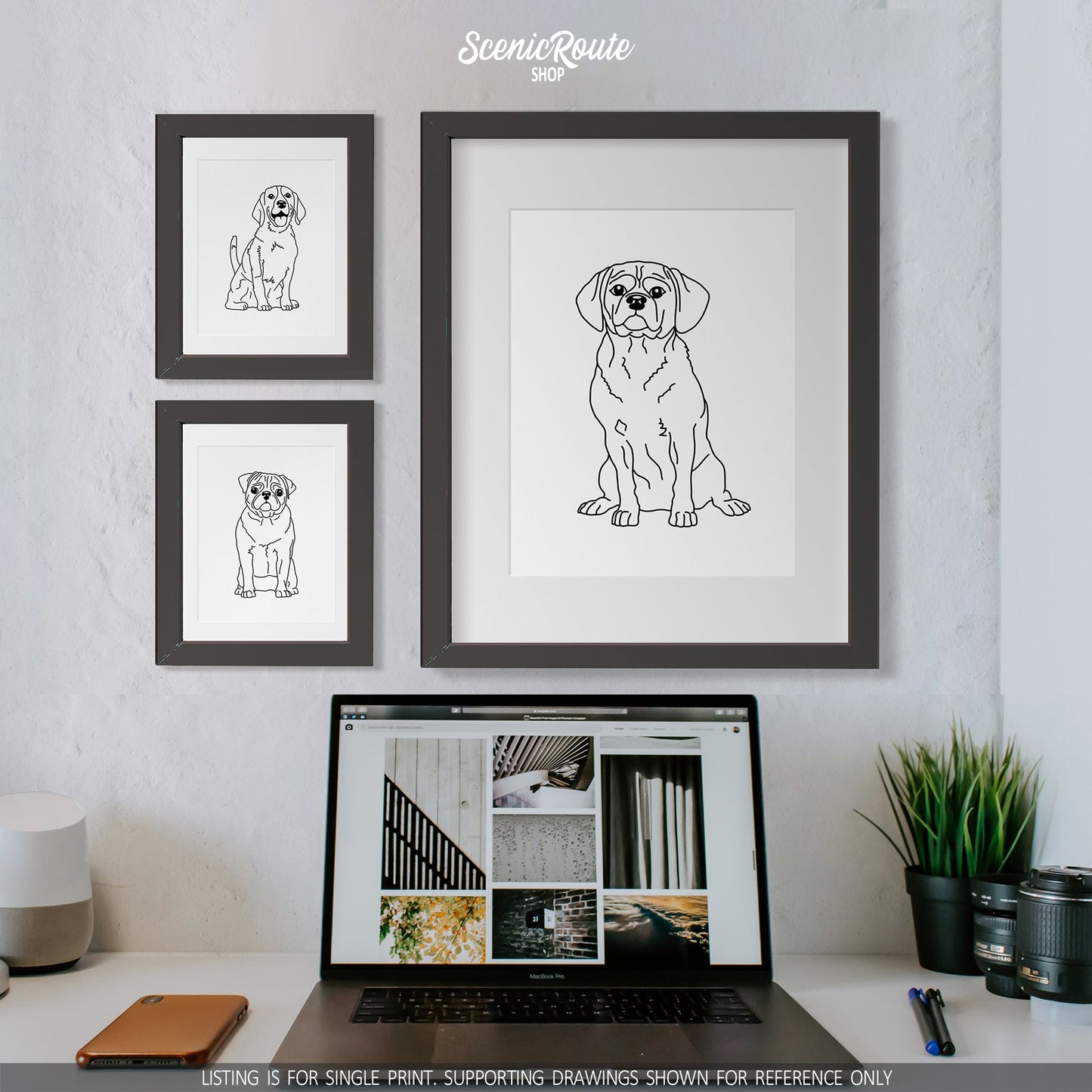 A group of three framed drawings on a white wall above a desk with a laptop. The line art drawings include a Beagle dog, a Pug dog, and a Puggle dog