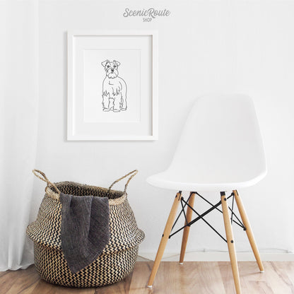 A framed line art drawing of a Schnauzer dog above a basket and chair