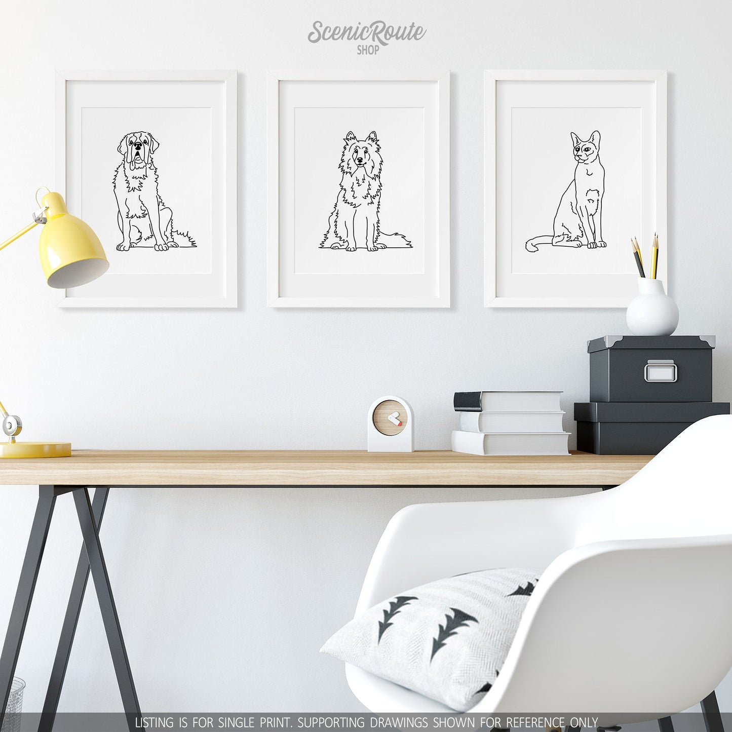 A group of three framed drawings on a white wall above a desk. The line art drawings include a Saint Bernard dog, a Shetland Sheepdog, and a Siamese cat