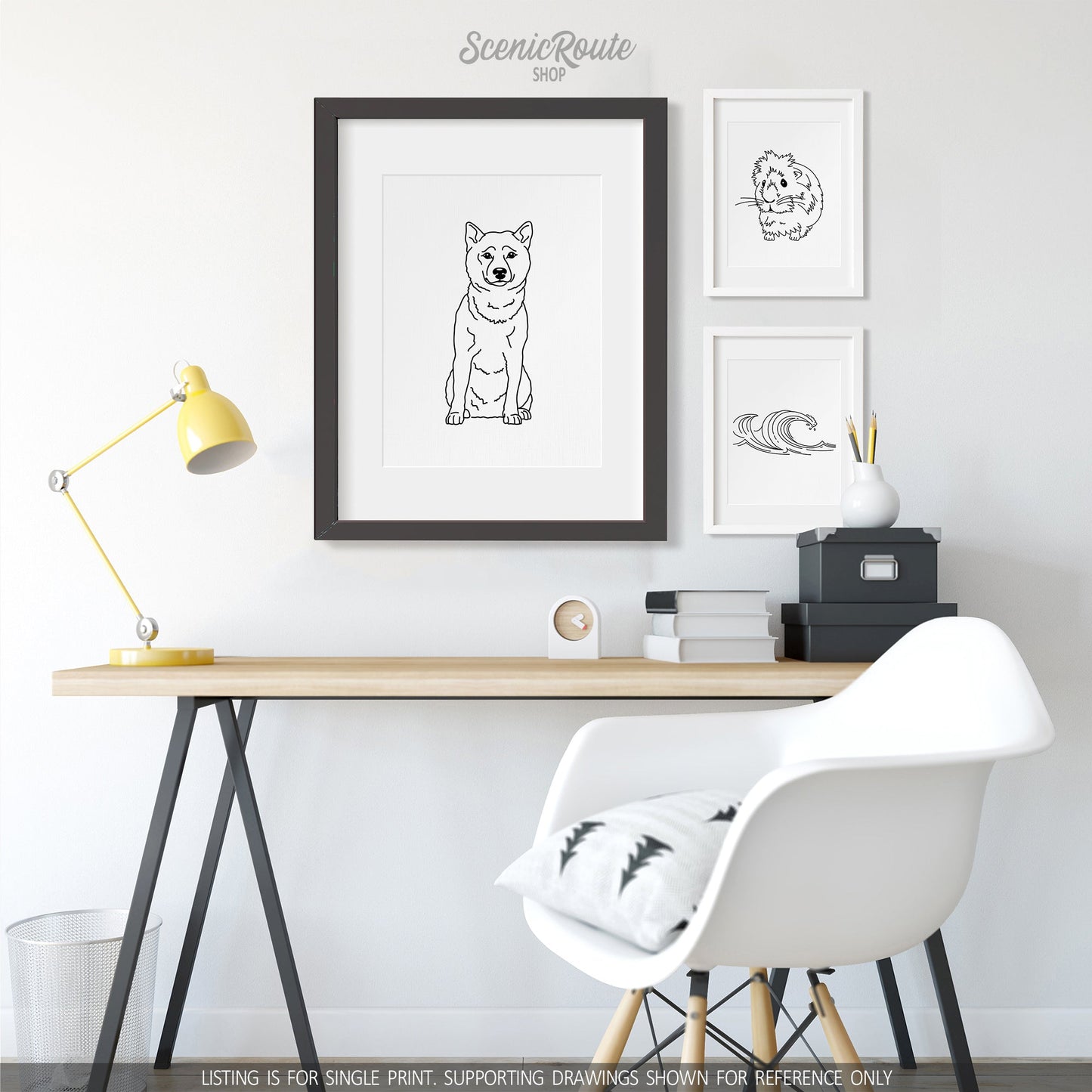 A group of three framed drawings on a white wall above a desk. The line art drawings include a Shiba Inu dog, a Guinea Pig, and Waves