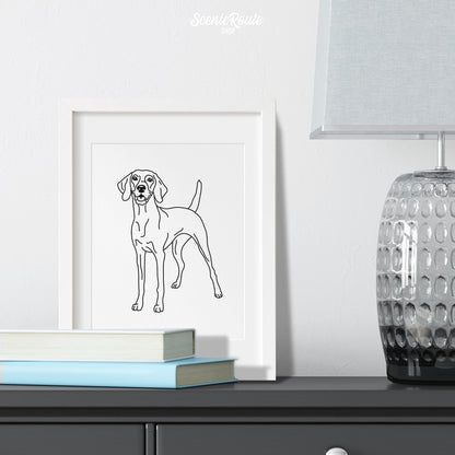A framed line art drawing of a Vizsla dog on a gray dresser with books and a lamp