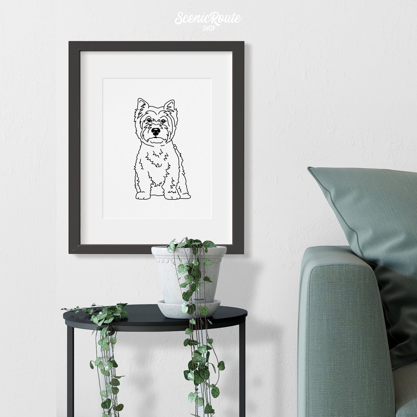 A framed line art drawing of a West Highland Terrier dog above a table with a plant next to a couch