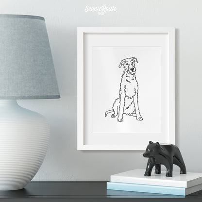 A framed line art drawing of a Wolfhound dog on a table with a lamp and figurine