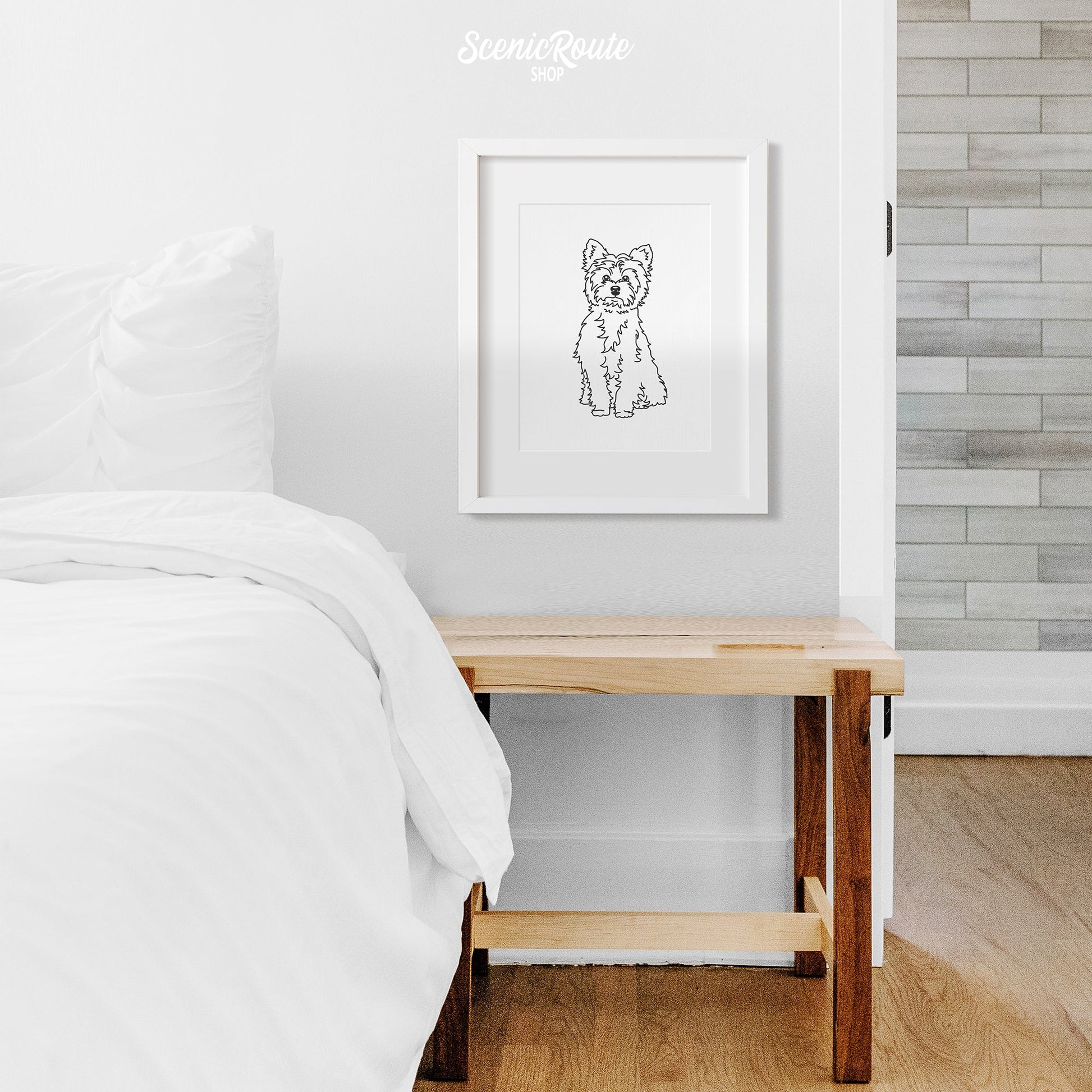A framed line art drawing of a Yorkshire Terrier dog on a wall above a nightstand next to a bed
