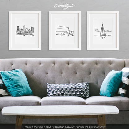 A group of three framed drawings on a wall above a couch. The line art drawings include the Milwaukee Skyline, a Lighthouse, and Sailing
