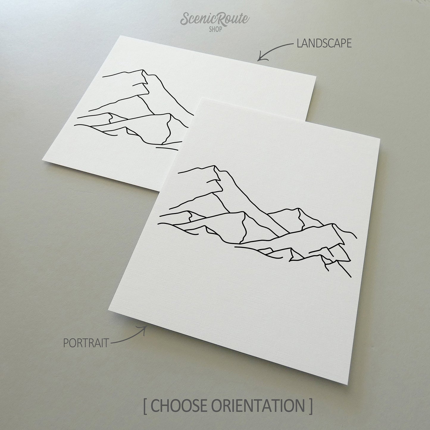Two line art drawings of A Mountain Range on white linen paper with a gray background.  The pieces are shown in portrait and landscape orientation for the available art print options.