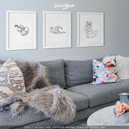 A group of three framed drawings on a white wall hanging above a couch with pillows and a blanket. The line art drawings include a Violin, Waves, and a Ragdoll cat