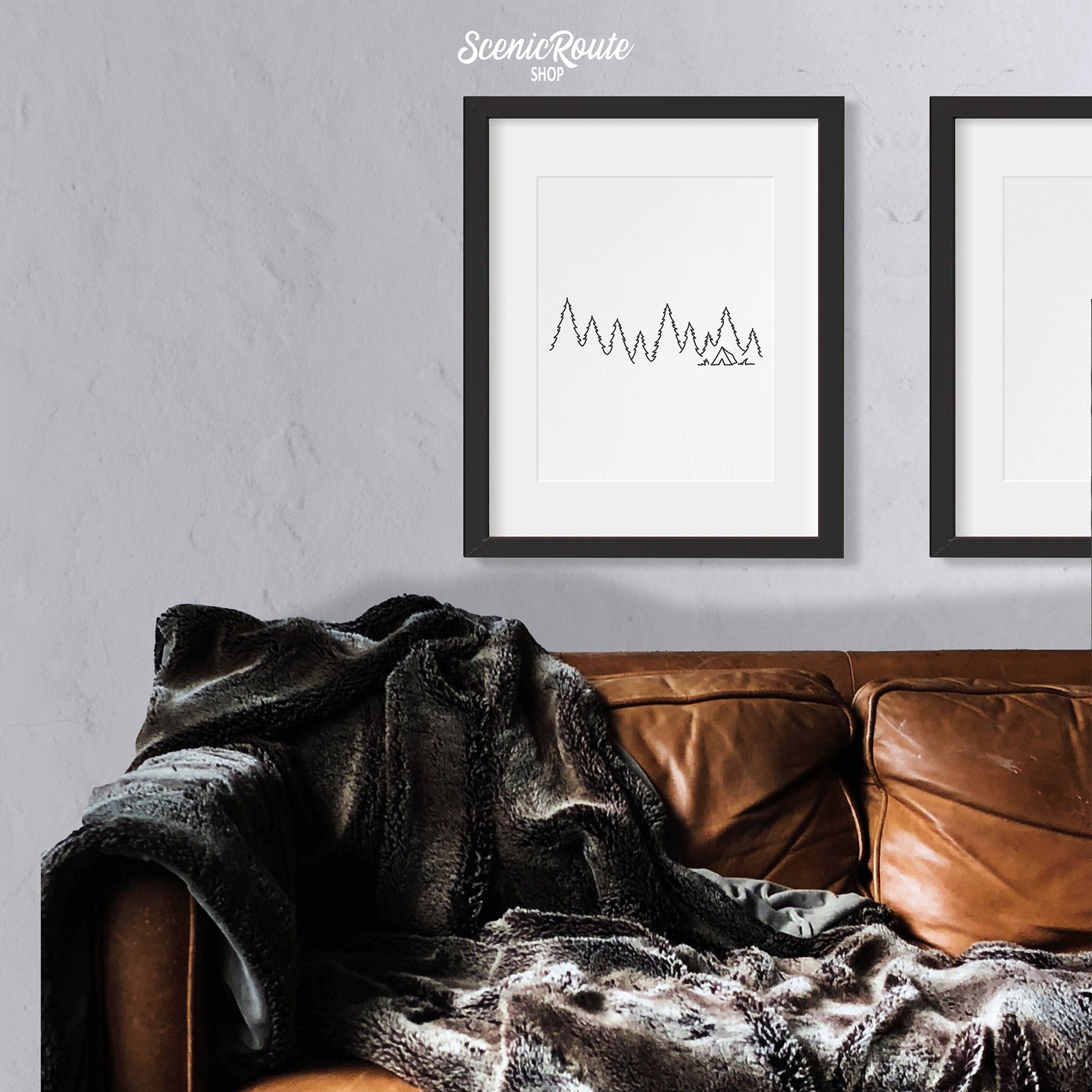 A framed line art drawing of Camping above a couch with a blanket