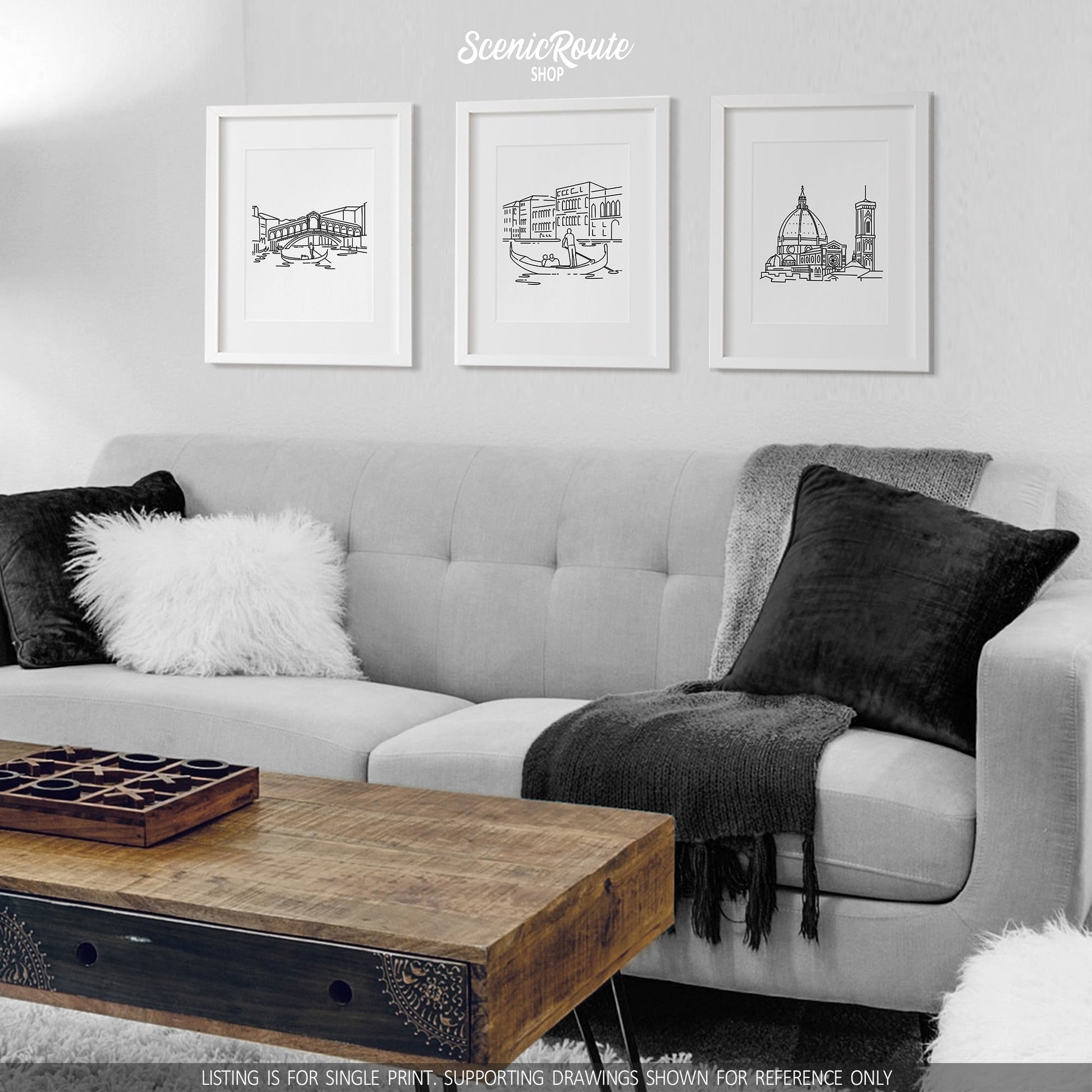 A group of three framed drawings on a white wall hanging above a couch with pillows and a blanket. The line art drawings include the Rialto Bridge, the Grand Canal, and the Florence Duomo