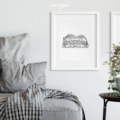 A framed line art drawing of the Brewers Ballpark above a couch and blanket