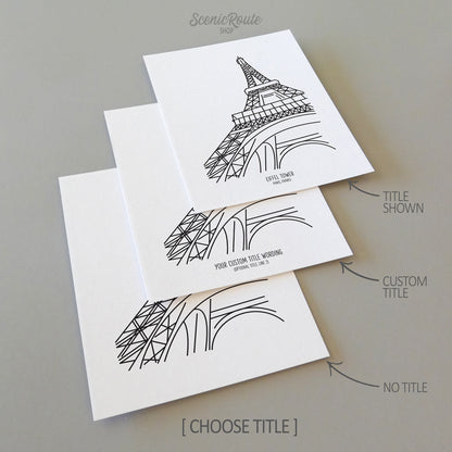 Three line art drawings of the Eiffel Tower in Paris France on white linen paper with a gray background.  The pieces are shown with title options that can be chosen and personalized.