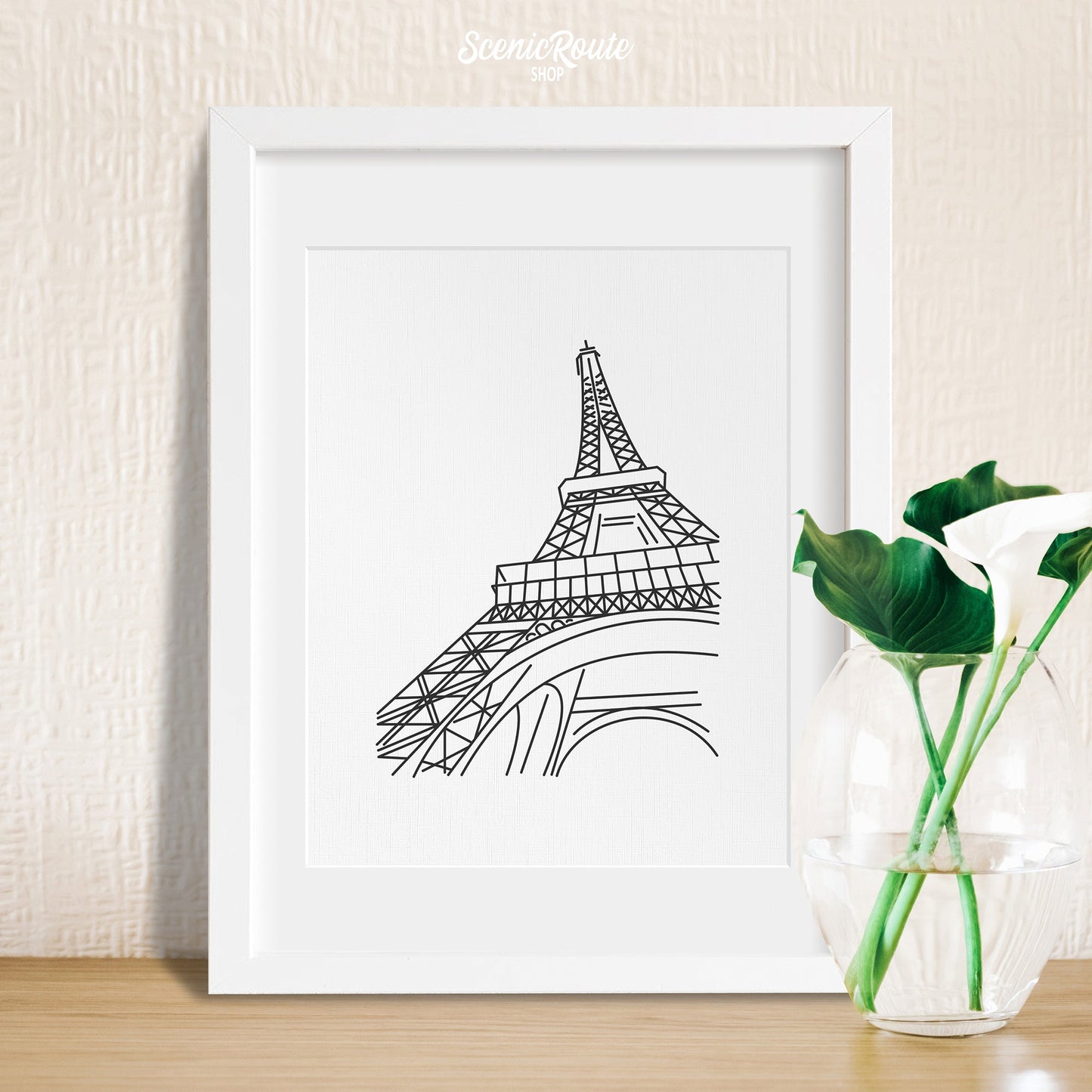 A framed line art drawing of the Eiffel Tower with a vase