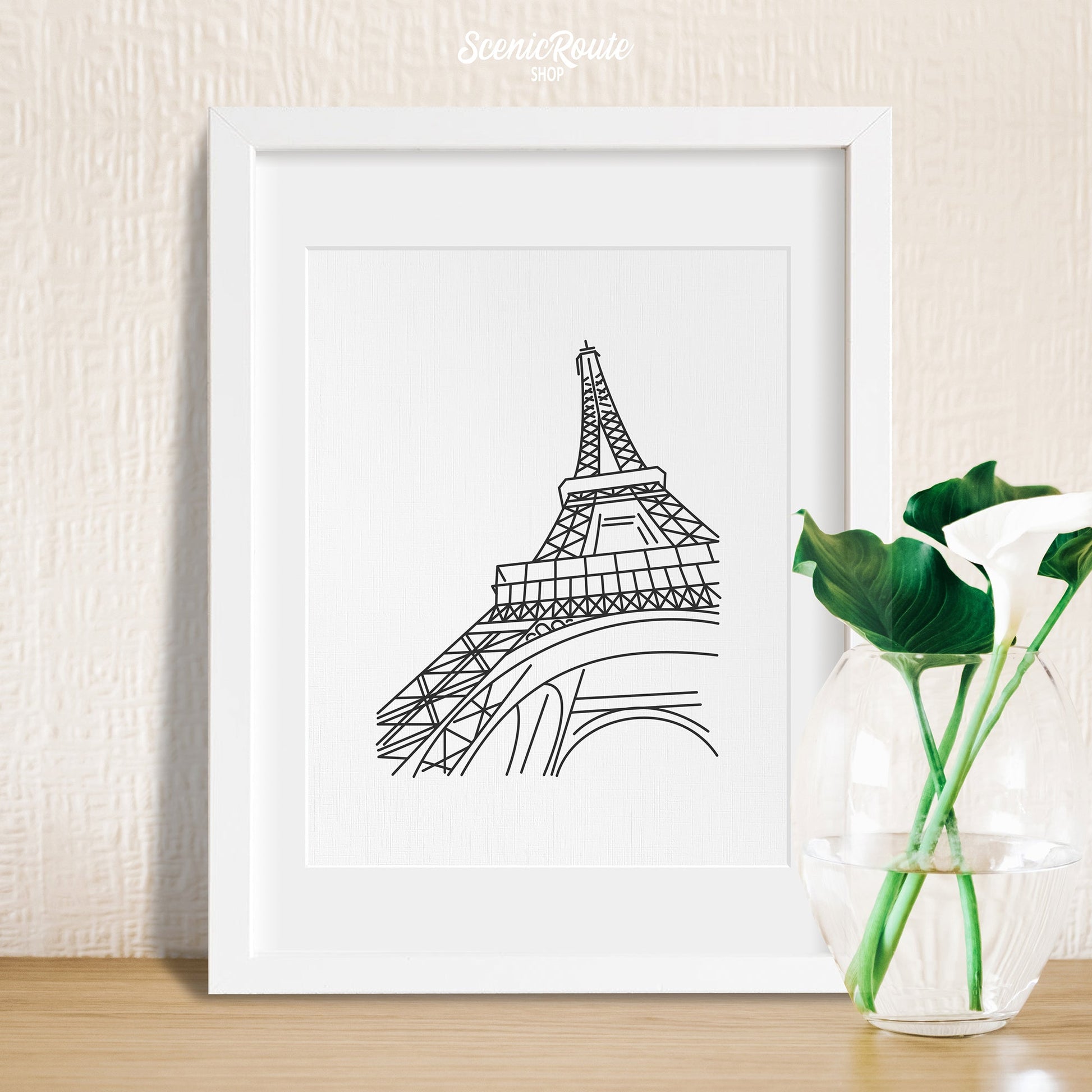 A framed line art drawing of the Eiffel Tower with a vase
