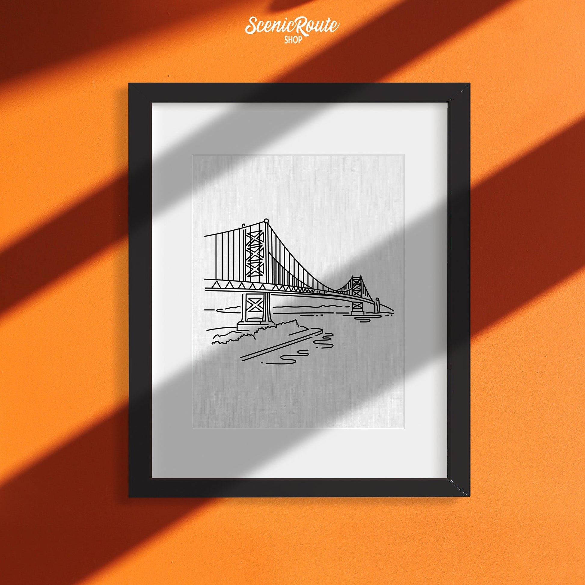 A framed line art drawing of the Ben Franklin Bridge on an orange wall