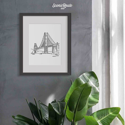 A framed line art drawing of the Golden Gate Bridge on a wall above a tropical plant