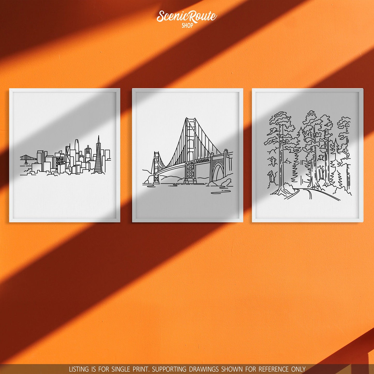 A group of three framed drawings on an orange wall. The line art drawings include the San Francisco Skyline, Golden Gate Bridge, and Redwood National Park