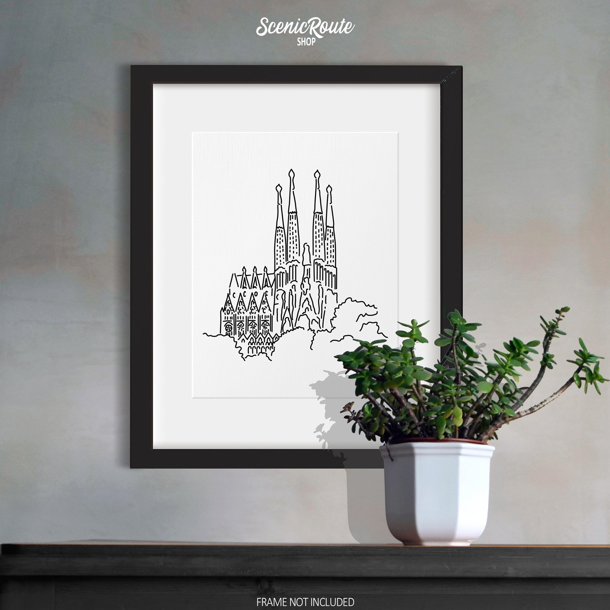 A framed picture of the Sagrada Familia hanging above a dresser with a potted plant