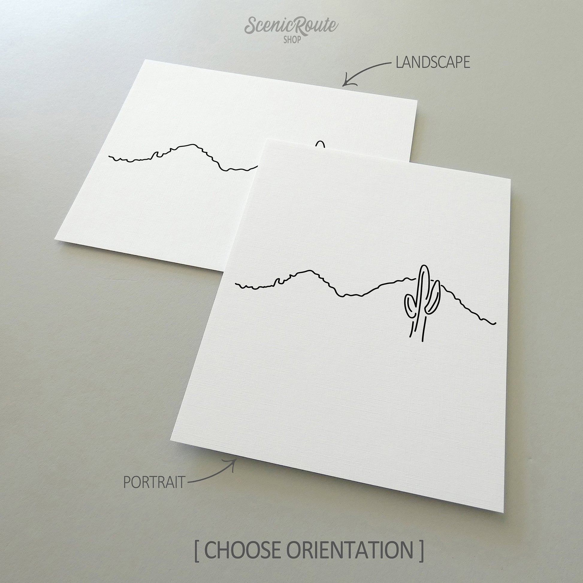 Two line art drawings of Camelback Mountain on white linen paper with a gray background.  The pieces are shown in portrait and landscape orientation for the available art print options.