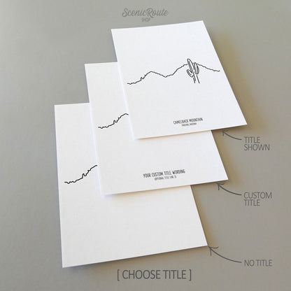 Three line art drawings of Camelback Mountain on white linen paper with a gray background.  The pieces are shown with title options that can be chosen and personalized.