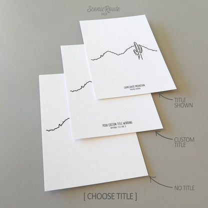 Three line art drawings of Camelback Mountain on white linen paper with a gray background.  The pieces are shown with title options that can be chosen and personalized.
